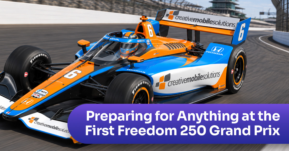 An INDYCAR racecar zooms around the track with orange and blue CMSI logos on the car